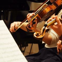 a woman playing the violin in front of a piano