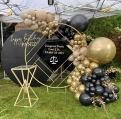 an arch made out of balloons and other items on the grass in front of a tent