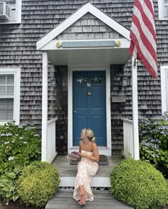 a woman sitting in front of a blue door with an american flag on the porch