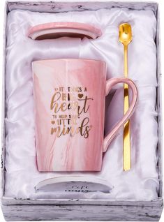 a pink and gold coffee mug in a gift box with a spoon next to it