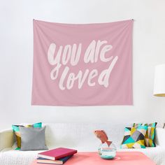 a pink wall hanging above a couch in a living room with pillows and blankets on it