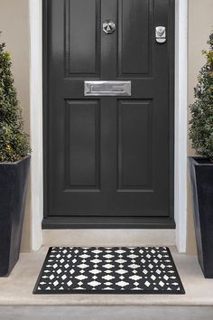 a black front door with potted plants on either side and a welcome mat in the middle