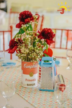 red flowers in a can on a table with empty wine glasses and utensils