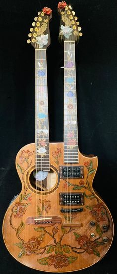 two guitars are sitting side by side on a black background, one is decorated with flowers and leaves