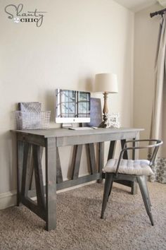 a wooden desk sitting in front of a window next to a chair and table with a computer on it