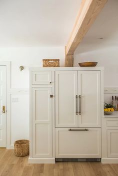 a white kitchen with wooden floors and cabinets in the corner, along with a basket on the counter