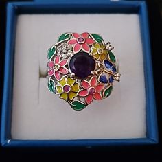 This Amethyst And Enameled Flower Ring Is Beautifully Crafted With A Round Amethyst Gemstone, Being The Center Of Attention It Is Designed Like A Bouquet Of Flowers And Is Beautifully Surrounded By Enameled Flowers, Leaves, And A Beautiful Butterfly. Each Is Accented With Different Gemstones Like Rubies, Yellow Sapphires, And White Zircons This Unique Ring Also Has A Signature Blue Sapphire In A Star Under The Beautiful Open Gallery Center Amethyst Is Approx 1.60 Ctw Gemstone Enamel Ring, Purple Jeweled Round Jewelry, Round Jeweled Enamel Jewelry, Flower-shaped Enamel Ring As Gift, Flower-shaped Enamel Ring For Gift, Floral Enamel Ring As Gift, Flower Shaped Enamel Ring As A Gift, Flower Shaped Enamel Ring For Gift, Round Multi-stone Enamel Jewelry