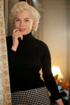 a woman standing next to a window with her hand on her chin and looking at the camera