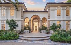 a large white house with lots of windows and plants in the front yard at sunset