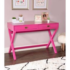 a pink desk with two pictures on the wall and a white rug in front of it