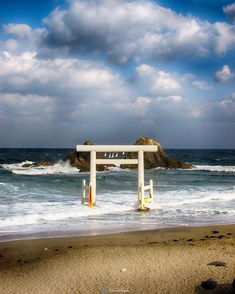 a white arch sitting on top of a sandy beach next to the ocean under a cloudy blue sky