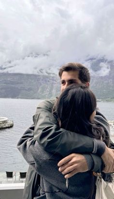 a man and woman embracing each other on a boat in front of the water with mountains behind them