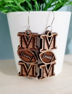 wooden earrings with the word football and an image of a football on it, sitting next to a potted plant