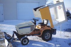 a small tractor with a trailer attached to it in front of a building and garage