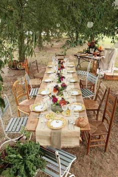 an outdoor dining table set up with plates and place settings for dinner under the trees