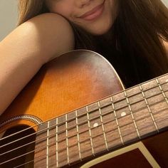 a close up of a person holding a guitar and posing for the camera with her hand on her shoulder