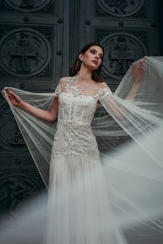 a woman in a white wedding dress with veils over her head and hands behind her back