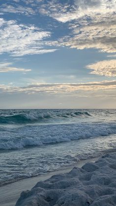 an ocean view with waves crashing on the shore and clouds in the sky above it