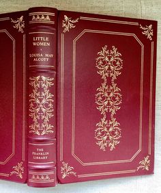 two red books sitting on top of a white cloth covered book case with gold trimmings