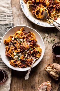 two plates of pasta with meat, cheese and tomato sauce on the table next to bread