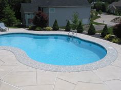 an above ground swimming pool surrounded by stone patios and lawn chairs with trees in the background