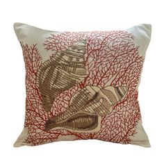 a red and white pillow with two seashells on the front, sitting on a coral