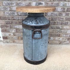 an old metal trash can with a wooden top sitting in front of a brick wall