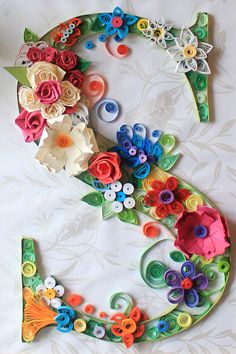 the letter e is made up of paper flowers and buttons on a white sheet with floral designs