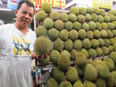 a man standing in front of a pile of durians at a market stall