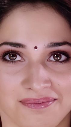 a close up of a woman with brown eyes and piercings on her forehead looking at the camera