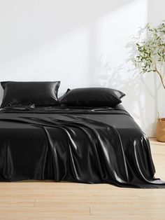 a bed with black sheets and pillows in a white room next to a potted plant