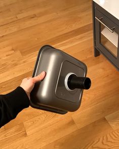 a person is holding a black and silver object in front of a wooden flooring area