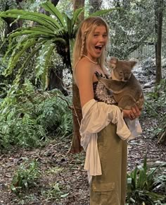 a woman holding a baby koala in her arms while standing next to a tree