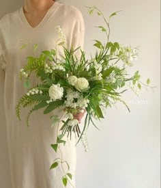 a woman in a white dress holding a bouquet of green and white flowers on her left hand