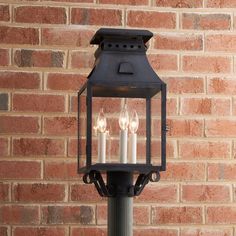 three candles are lit on the side of a lamp post in front of a brick wall