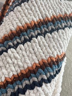 a crocheted blanket on top of a couch next to a pillow with an orange, white and blue design