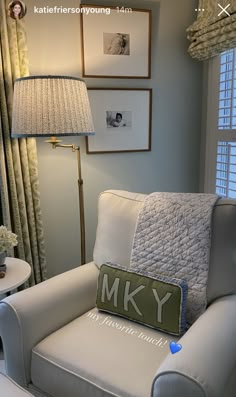 a white chair sitting in front of a window next to a lamp and pictures on the wall