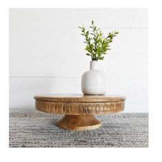 a white vase sitting on top of a wooden stand with a plant in the middle