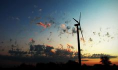 the sun is setting behind some wind turbines