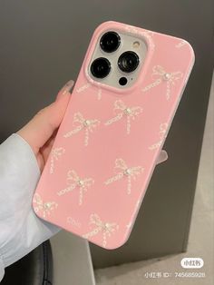 a pink phone case with bows and pearls on the back is held up by a woman's hand