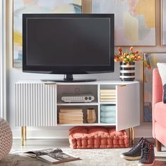 a flat screen tv sitting on top of a white entertainment center next to a pink couch