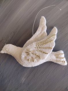 a white bird ornament with gold beads on it's body and wings