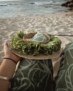 a person sitting on the beach holding a plate with some food in front of them