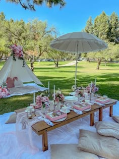 a picnic table set up with pink flowers and white umbrellas for an outdoor party