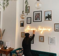 a woman standing in front of a wall with neon signs on it and hanging plants