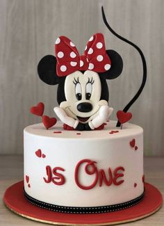 a cake with a minnie mouse on top that says it's one in red and white hearts