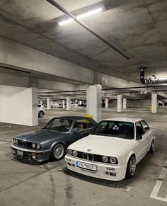 two cars parked in a parking garage next to each other on the ground and one is white