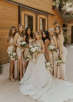 a group of women standing next to each other in front of a wooden building holding bouquets