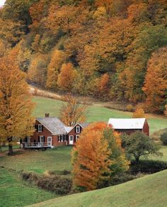 a red house surrounded by trees with fall foliage on the hillsides in the background