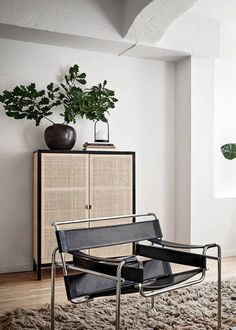 a black chair sitting on top of a rug next to a wooden cabinet and potted plant